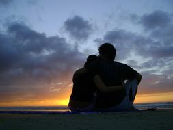 Silhouette of the sitting couple on the beach, at colorful and beautiful sunset among the clouds