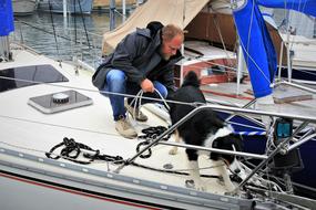 Man with beautiful and cute, black and white dog on the sailboat, on the water in Switzerland