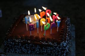 Close-up of the beautiful Birthday cake with colorful, burning candles, among the darkness