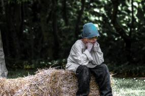 Boy in cap, sitting on the straw, among the plants