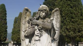 Statue of a sad angel in the cemetery near the trees