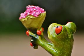 ceramic frog with bouquet on blurred background