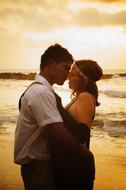 Couple kissing on the sandy beach, at sunset with clouds