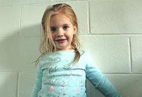 Portrait of the cute, smiling, blonde child girl near the white wall in lights and shadows