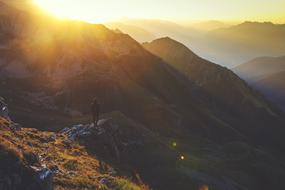 a guy standing alone on a mountain during sunset