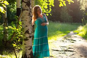 pregnant woman in a turquoise dress by the birch