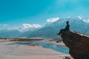 lonely man sits on a rock near a mountain river