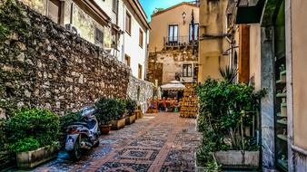 Beautiful landscape of the colorful alley with the plants and scooter and people, among the buildings in Sicily, Italy