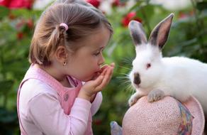 Cute girl, blowing kiss to the colorful, cute and beautiful rabbit, near the colorful and beautiful plants with the flowers