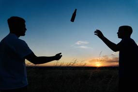 Silhouettes of the people, playing with the bottle, among the grass, at colorful and beautiful sunset