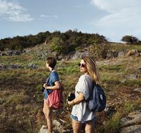 Girls with backpacks, walking on the beautiful and colorful mountains with plants, under the sky with clouds