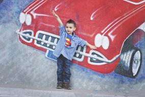 Boy in "Superman" shirt near the wall with the colorful car graffiti