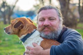 Portrait of the smiling man with the beard and moustache, with the colorful, cute and beautiful dog, among the colorful plants