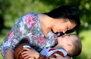 Smiling mom with the cute, smiling son with beautiful and cute, brown Teddy Bear, among the green plants