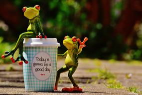 Cute, colorful and beautiful, shiny figures of the frogs and coffee cup among the colorful plants, in sunlight
