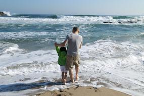 dad and daughter on the beach against the background of sea waves