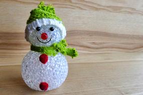 Beautiful, shiny, smiling snowman decoration in colorful clothes, on the wooden surface