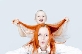 Cute, blonde son playing with the ginger hair of the mother