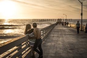 couple in love near the fence on the pier during sunset