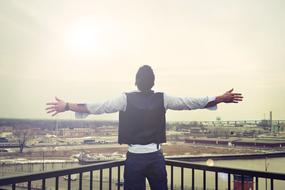 man with outstretched arms on the rooftop above the city