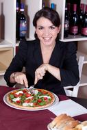 Smiling woman in black jacket, eating colorful and beautiful pizza, near the bottles