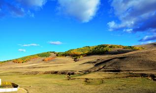 Beautiful and colorful landscape of the hills with plants in sunlight, under the blue sky with clouds, in the autumn