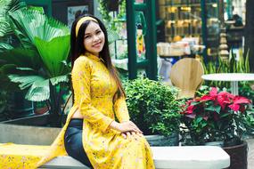 pretty asian girl in yellow dress sits near ornamental plants