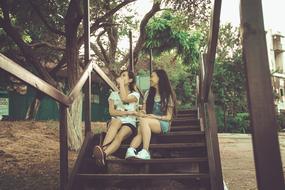 two girlfriends laugh and sit on a wooden staircase in Vietnam