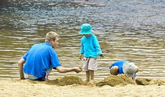 Father and children, playing in sand, near the colorful water with ripple