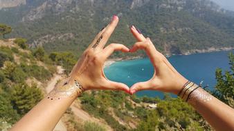 Woman showing heart at background with the beautiful mountains with green plants and lake