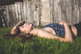 Profile portrait of the laying, beautiful girl, on the green grass, near the wooden wall