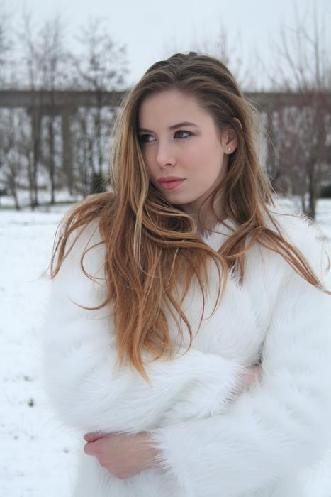 Beautiful, blonde girl in white coat, among the beautiful, snowy landscape