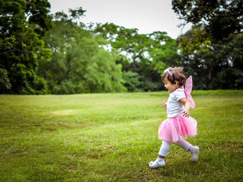 Cute girl in colorful princess costume, walking on the lawn, among the green trees