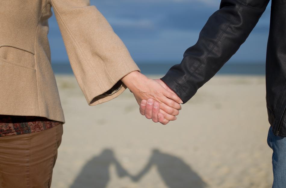 Close-up of he couple, holding hands together, on the beautiful sandy beach