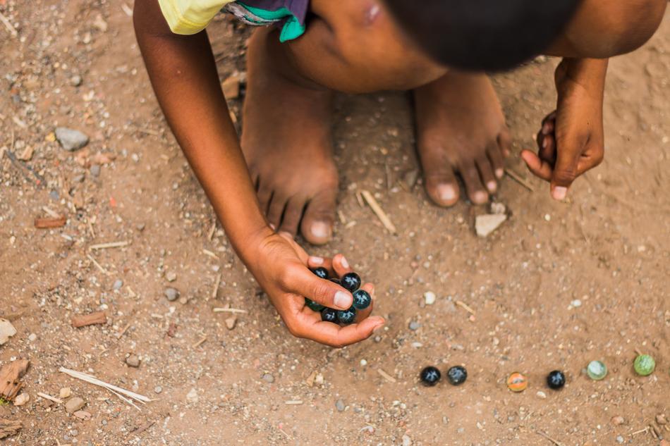 Indian kid, playing with the colorful, glossy marbles on the ground