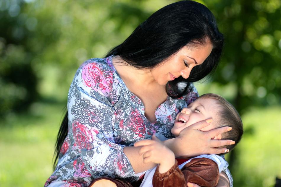 Smiling mother with the son, among the green plants in light