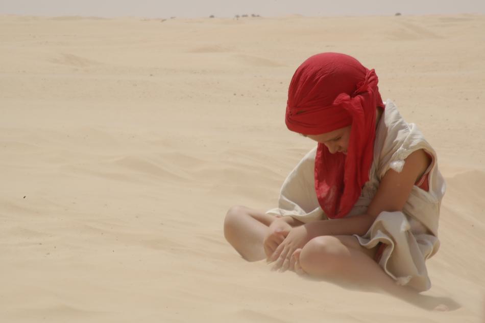 a child in a red scarf on the sand in the desert