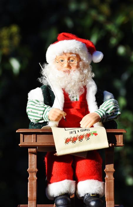 Figure of Santa Claus, writing on the paper, at background with green plants
