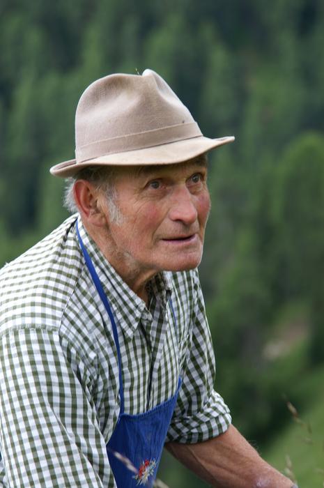 Portrait of the senior man in hat, among the beautiful, green plants, on the Dolomites in Italy
