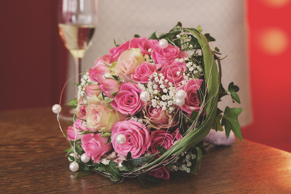 Close-up of the beautiful bridal bouquet with the colorful flowers, near the glass of champagne, on the table