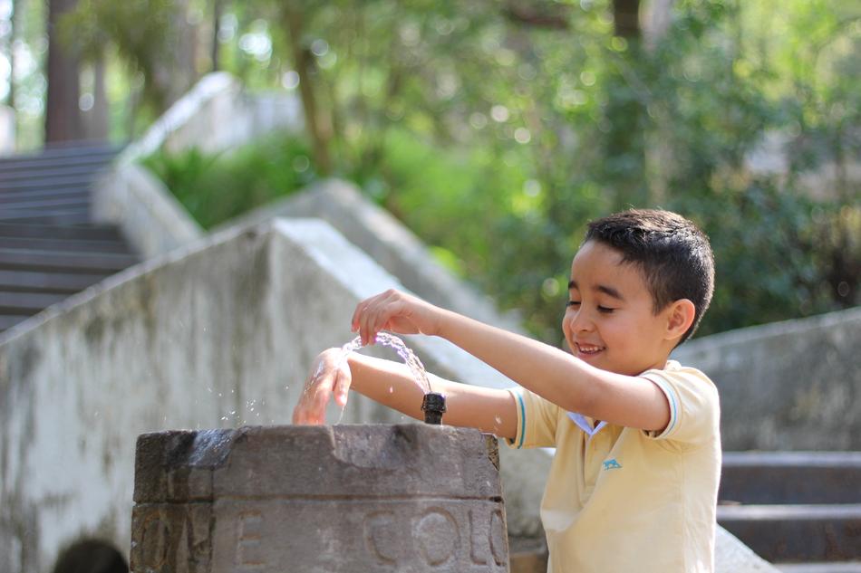 the boy put his hands in the water source in the park