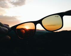 Close-up of the colorful sunglasses in hands, at dark landscape at sunset