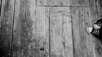 Black and white photo with close-up of the wooden floor and person in shoes