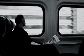 black and white, a man with a newspaper rides a train