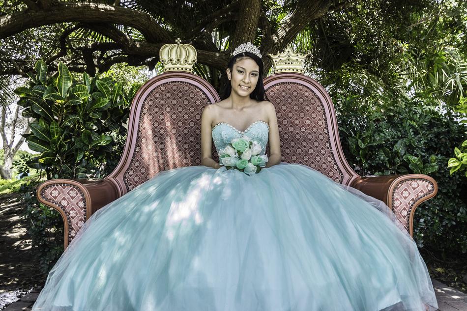 Smiling woman in dress, with the bouquet of flowers, sitting on the sofa at Quinceanera