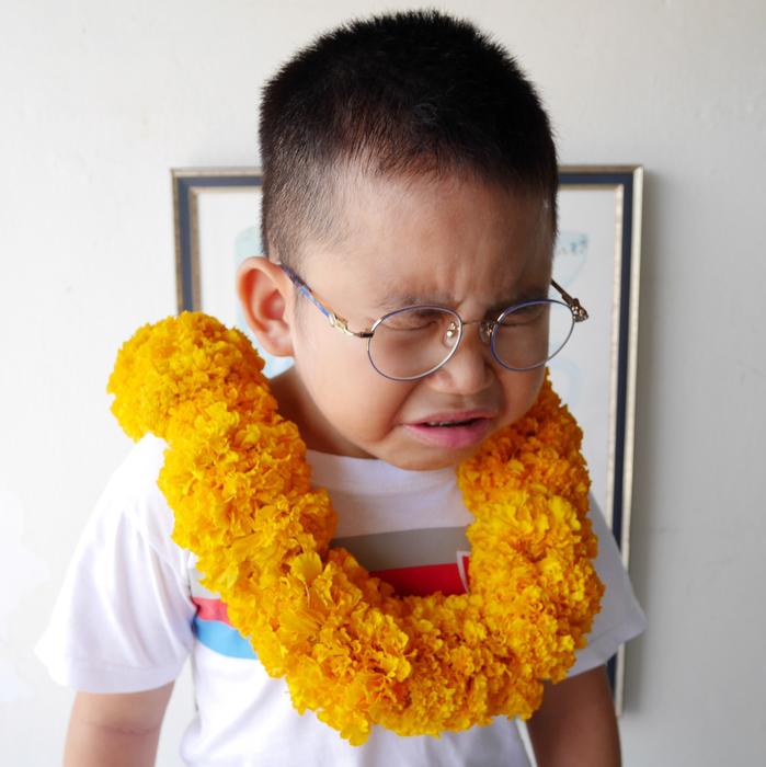 Portrait of the crying child with glasses and orange marigold flowers