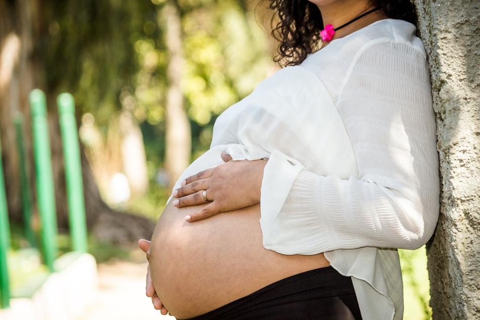 Pregnant woman posing near the tree, at blurred background with plants