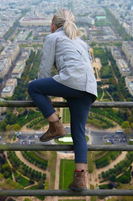 Back view of the blonde girl climbing on the railing, at background with cityscape