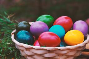 colorful shiny easter eggs in wicker bowl on blurred background