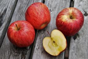 three red apples and half on a wooden table